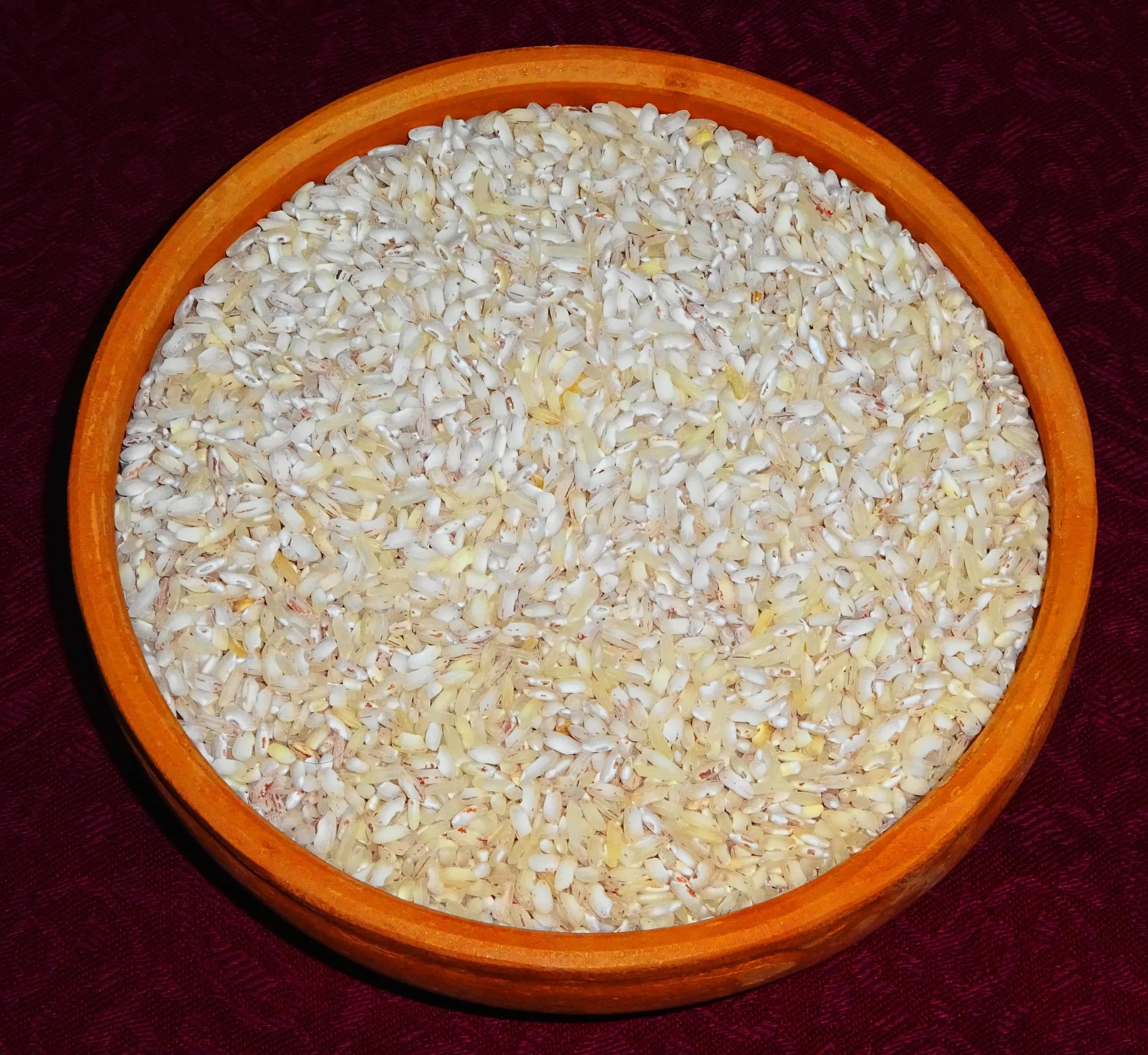 A bowl of uncooked Kerala Matta rice on a dark cloth