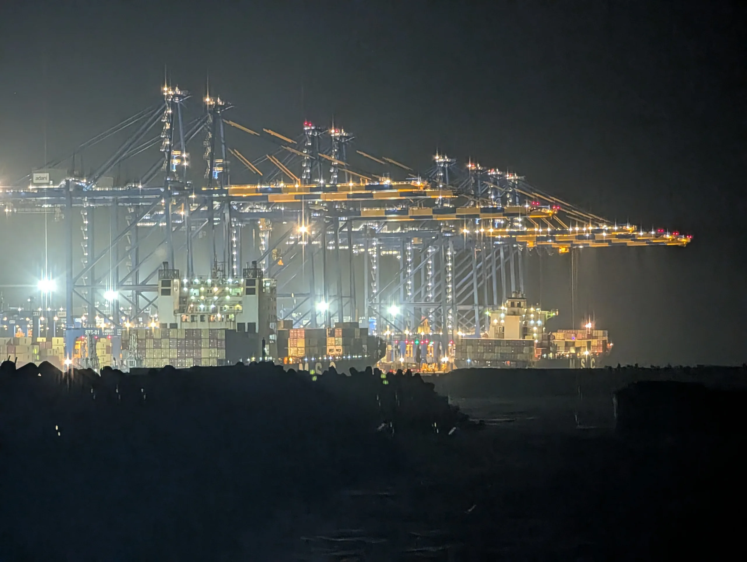Container cranes and a berthed vessel lit up at night at Vizhinjam port, Kerala